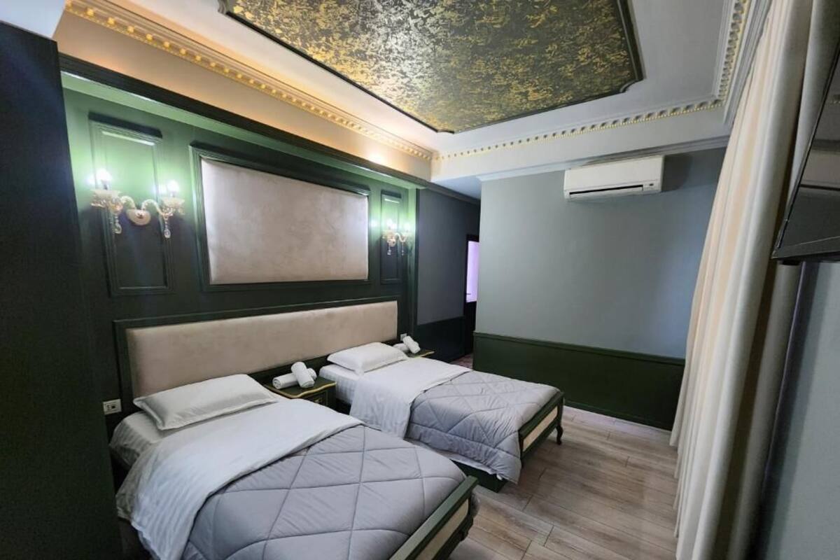 A hotel room with two beds, a large mirror, a flat-screen TV, and an air conditioning unit.