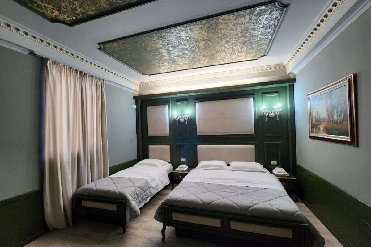 A room with two beds, a large painting on the wall, and a ceiling with a decorative pattern.