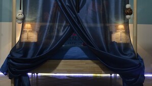 Una cama con cortinas azules, dos lámparas de noche y una alfombra estampada.