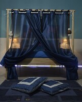 Una cama con cortinas azules, dos lámparas de noche y una alfombra estampada.
