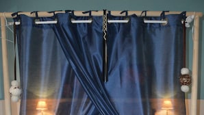 Una cama con una colcha azul y almohadas a juego, una cortina azul y una alfombra pequeña con un diseño geométrico.