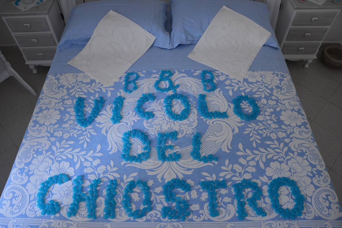 Una cama con una colcha azul estampada con flores y un arreglo decorativo que dice "B&V VICOLO DEL CHO STRO".