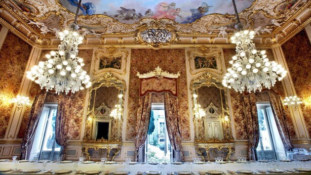 Una habitación opulenta con detalles dorados ornamentales, grandes candelabros y un espejo imponente.