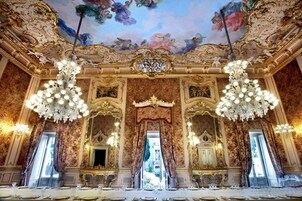 Una habitación opulenta con detalles dorados ornamentales, grandes candelabros y un espejo imponente.