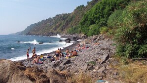 Una playa rocosa con gente tomando el sol y nadando, rodeada de exuberante vegetación y vistas al océano.