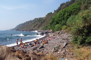 Una playa rocosa con gente tomando el sol y nadando, rodeada de exuberante vegetación y vistas al océano.