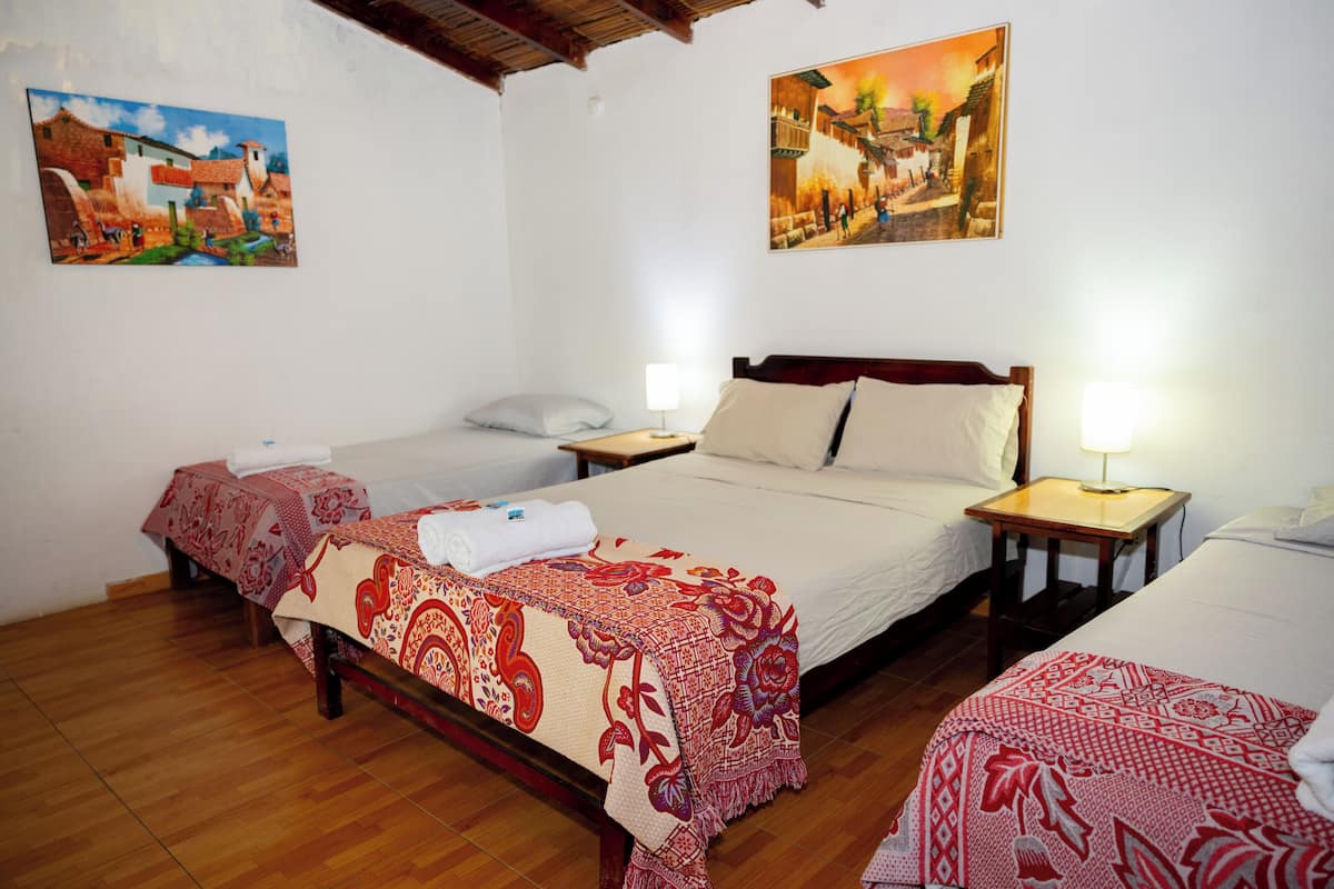 Una habitación de hotel con dos camas, piso de madera y dos cuadros en las paredes.