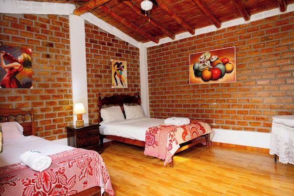 Una habitación con dos camas, una pared de ladrillo, suelo de madera y obras de arte en las paredes.