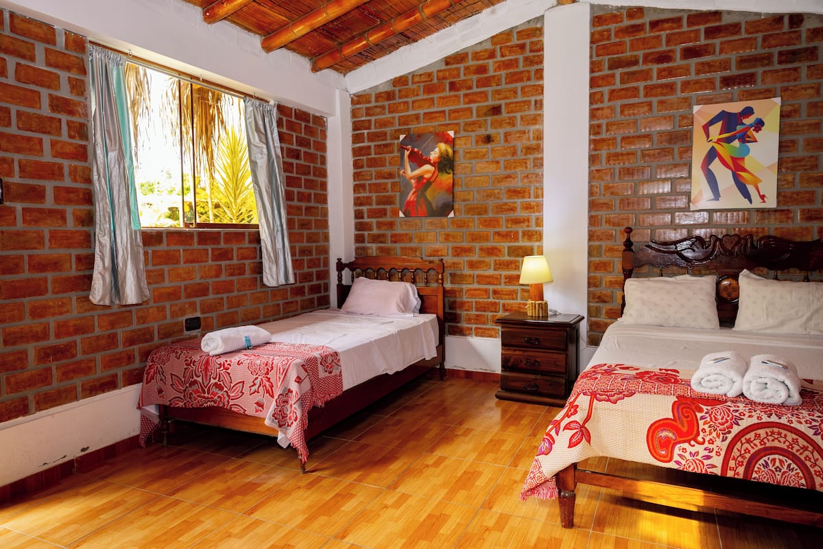 Una habitación con dos camas, una pared de ladrillo y suelo de madera.