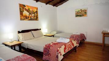 A hotel room with three beds, wooden floors, and two paintings on the walls.