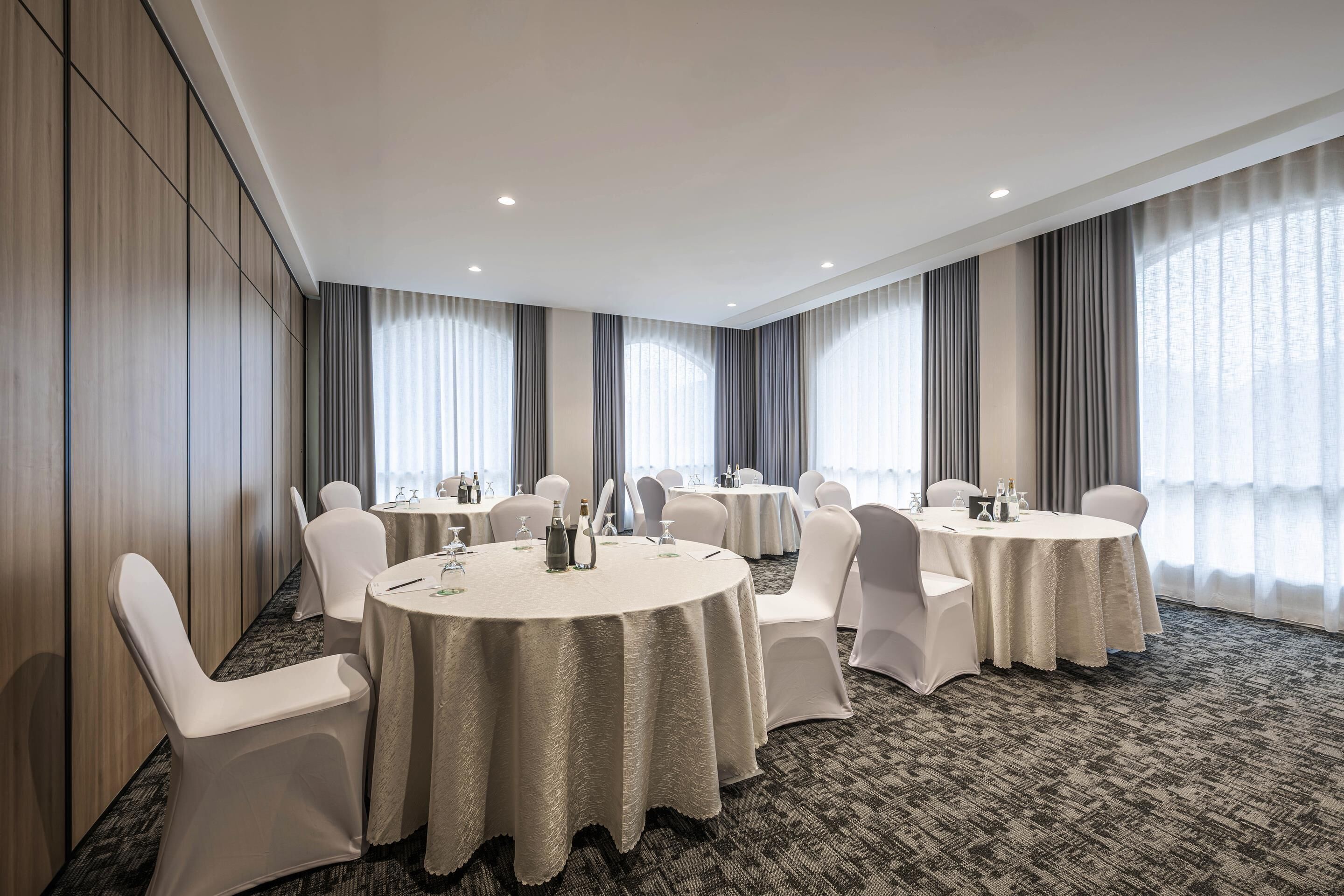 Un salón de conferencias con mesas redondas, sillas blancas y suelo alfombrado.