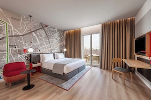A hotel room with a bed, a desk, a chair, a map on the wall, and a view through the window.