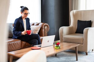 Une personne est assise sur un canapé en cuir marron, un ordinateur portable est posé sur ses genoux et une tasse rouge se trouve sur une table basse en bois.