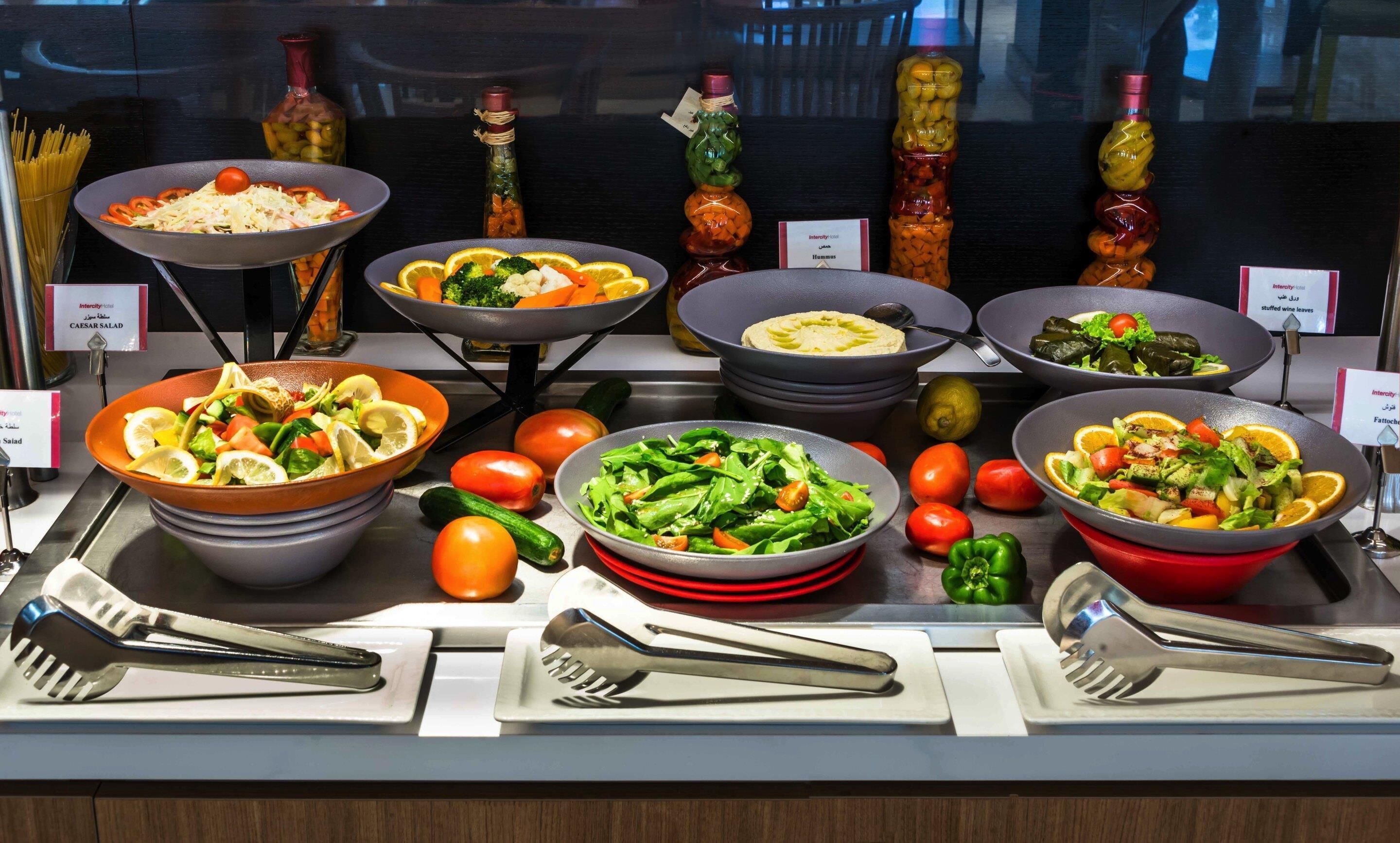 A buffet with various dishes, including Caesar salad, stuffed grape leaves, and a salad with orange slices.