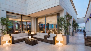 A modern outdoor seating area with wicker furniture and lamps, large windows, and potted plants. - IntercityHotel Riyadh Malaz (Riyadh)