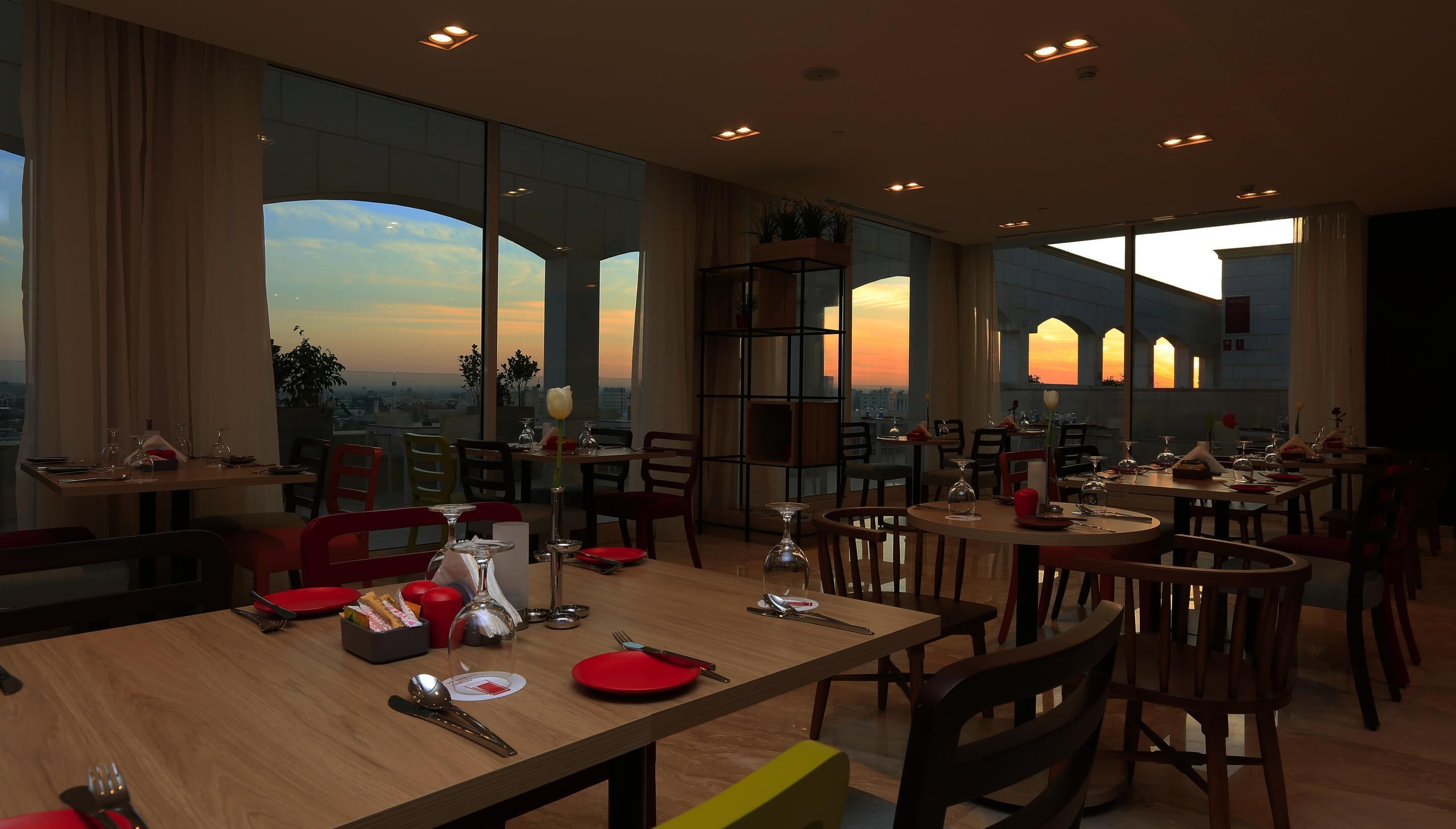 Un restaurant doté de nombreuses tables, de chaises et de grandes fenêtres offrant une vue sur la ville.