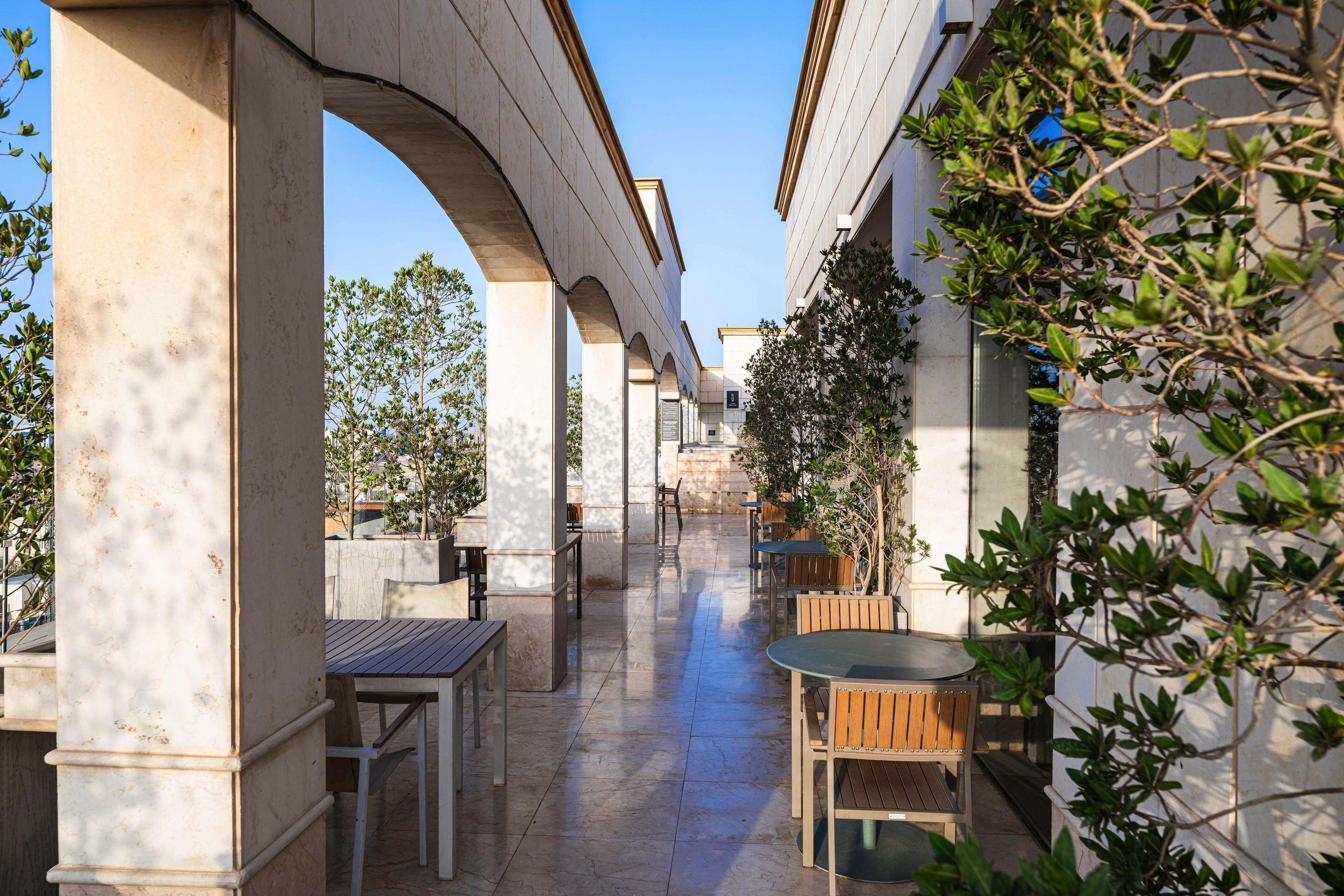 An outdoor patio area with tables and chairs, a covered walkway, and greenery.