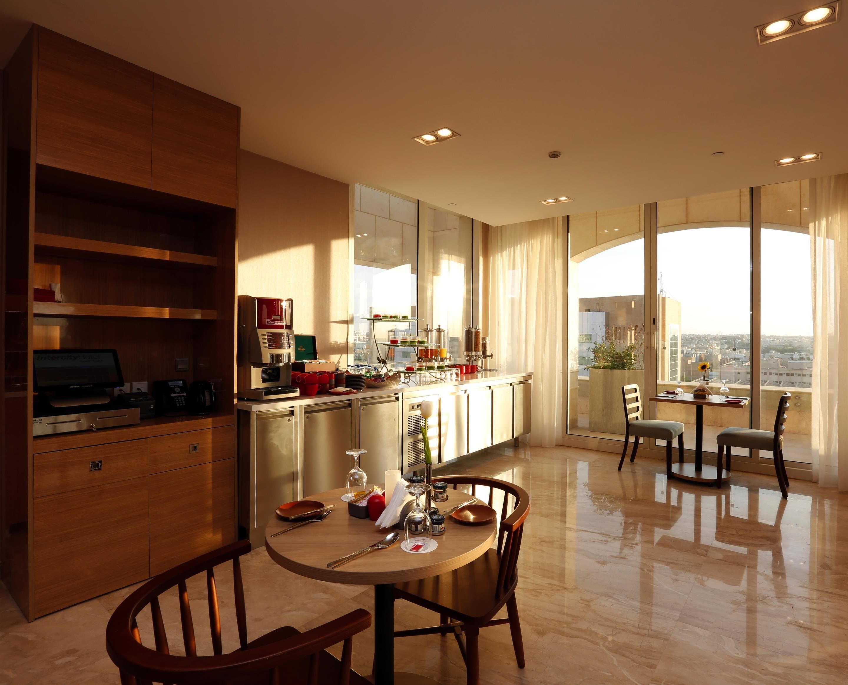 A modern kitchen with a dining area, large windows, and a city view.