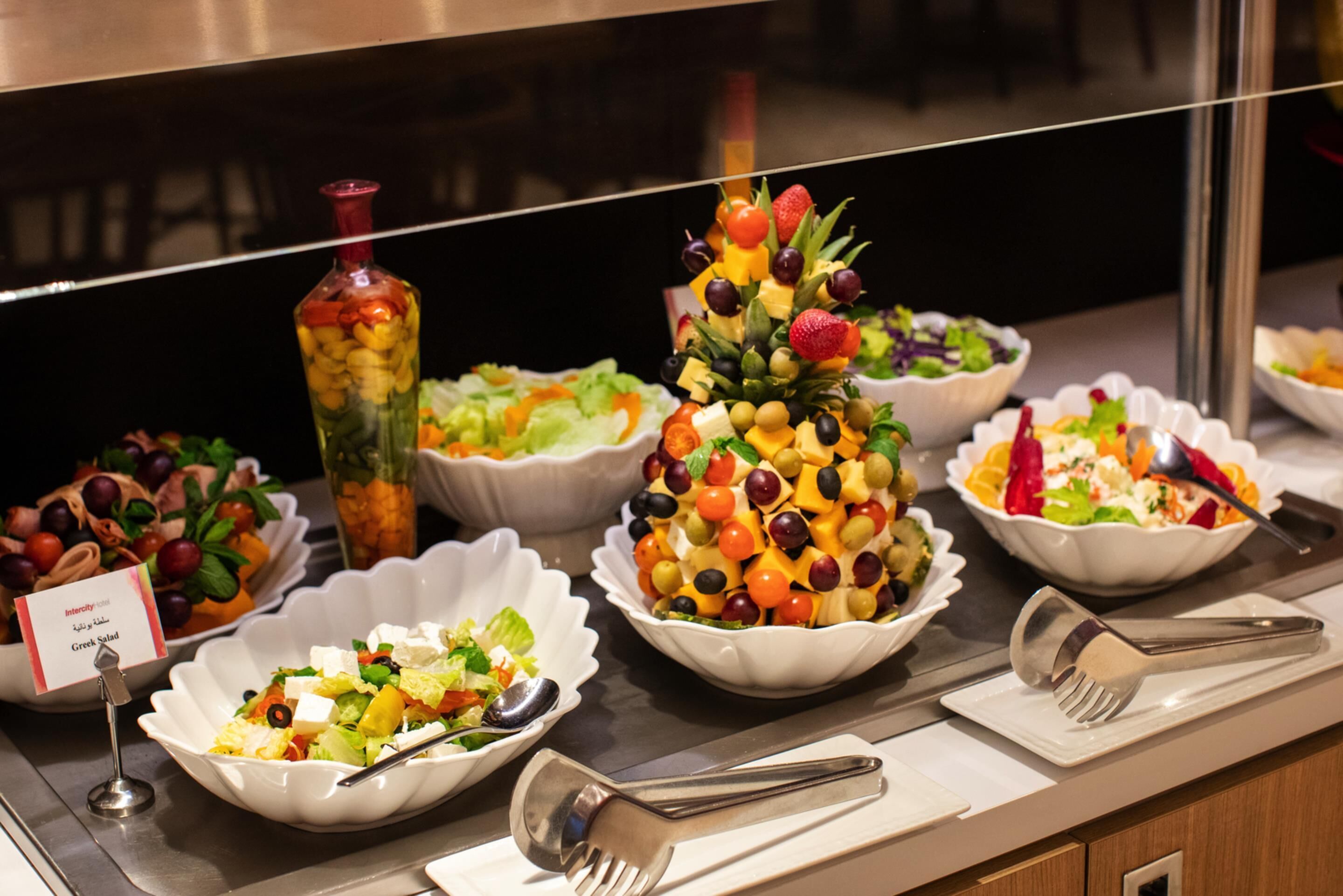 A buffet with various dishes including a fruit salad, Greek salad, and a salad with red peppers.