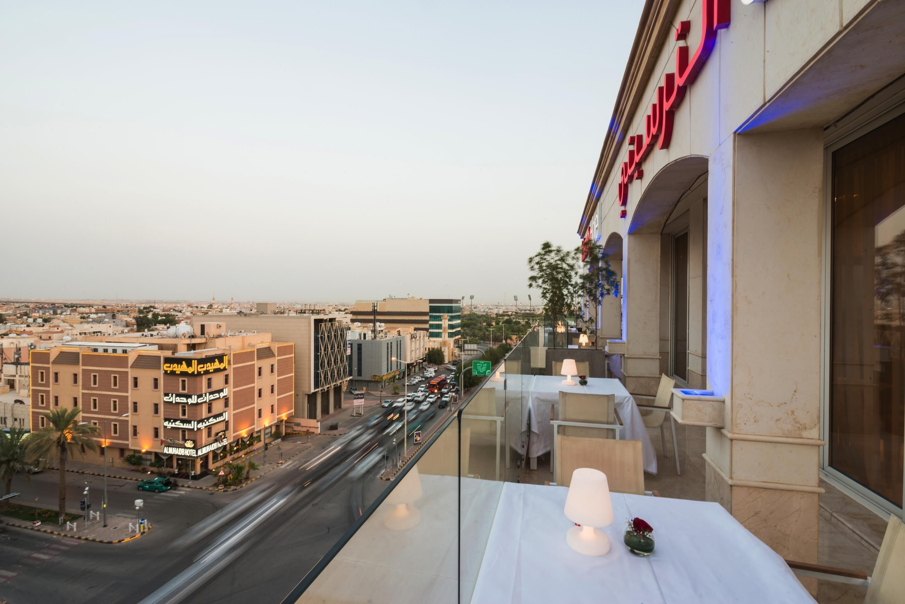 Un balcón de hotel con vistas a la ciudad, incluyendo un edificio hotelero con señalización árabe.