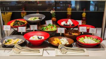 A buffet with labeled dishes including stuffed wine leaves, hummus, mix cheese, fruit salad, and egg salad.