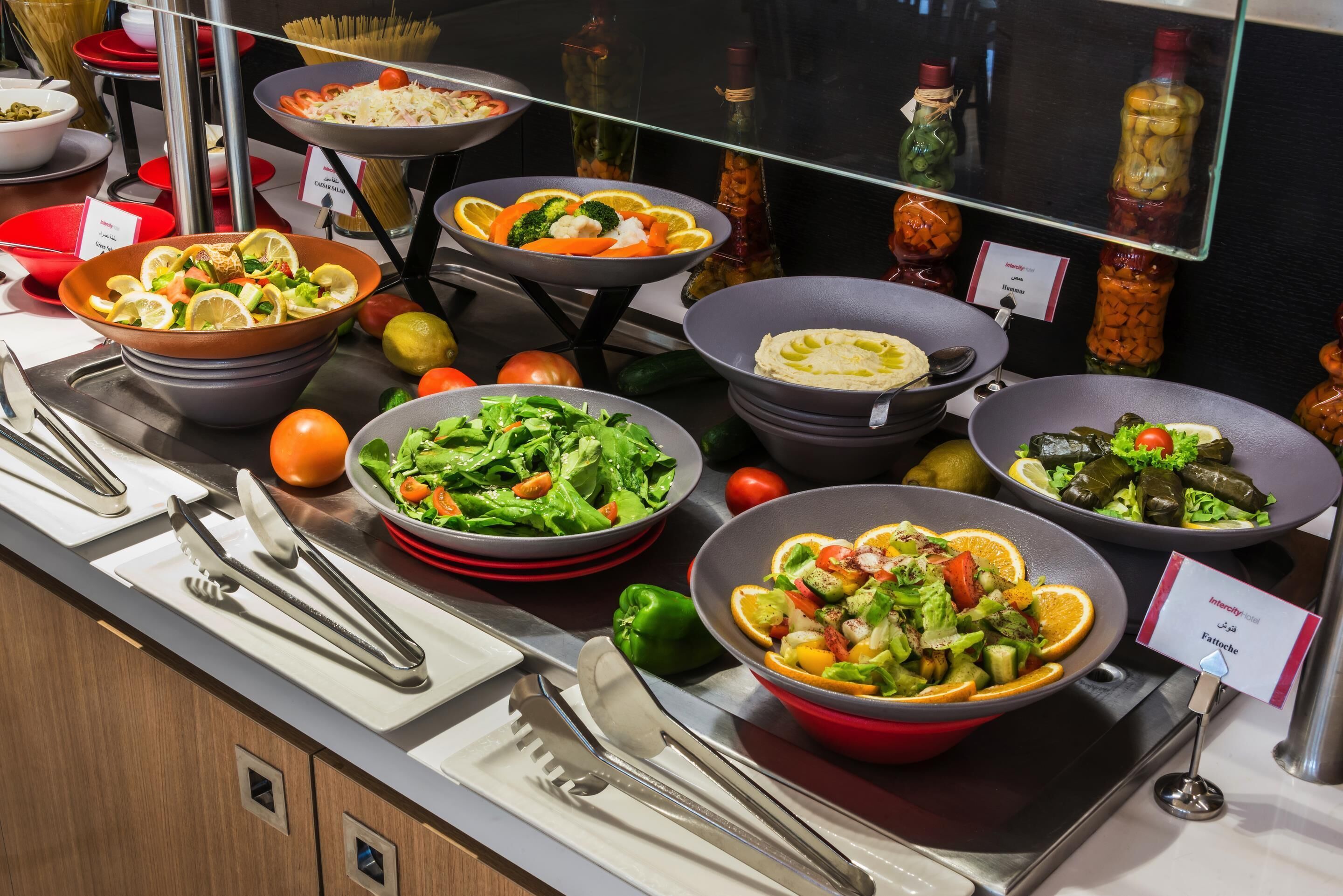Un bufé con diversos platos, entre ellos ensaladas y arroz, dispuesto en un mostrador con utensilios de servicio.