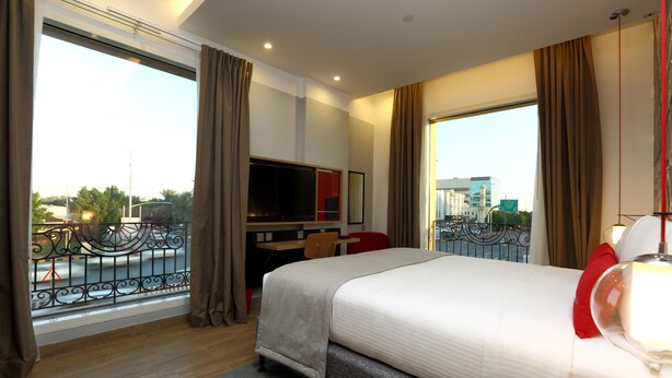 A hotel room with a large bed, a TV, a desk, and a view of the city. - IntercityHotel Riyadh Malaz (Riyadh)