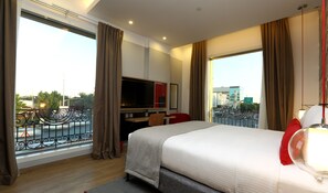Habitación de hotel con una cama grande, televisión, escritorio y vistas a la ciudad.