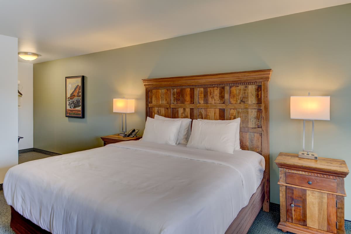 A large bed with a wooden headboard, two bedside tables with lamps, and a framed picture on the wall.