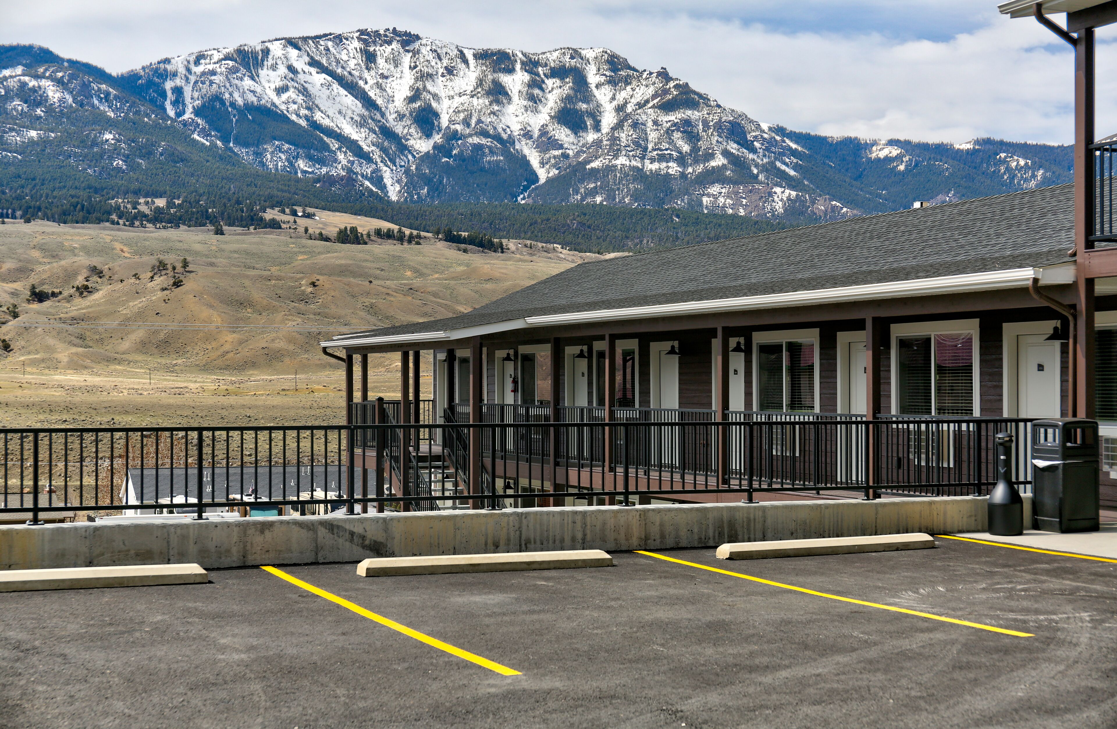 A building with a balcony overlooking a parking area, with mountains in the background.
