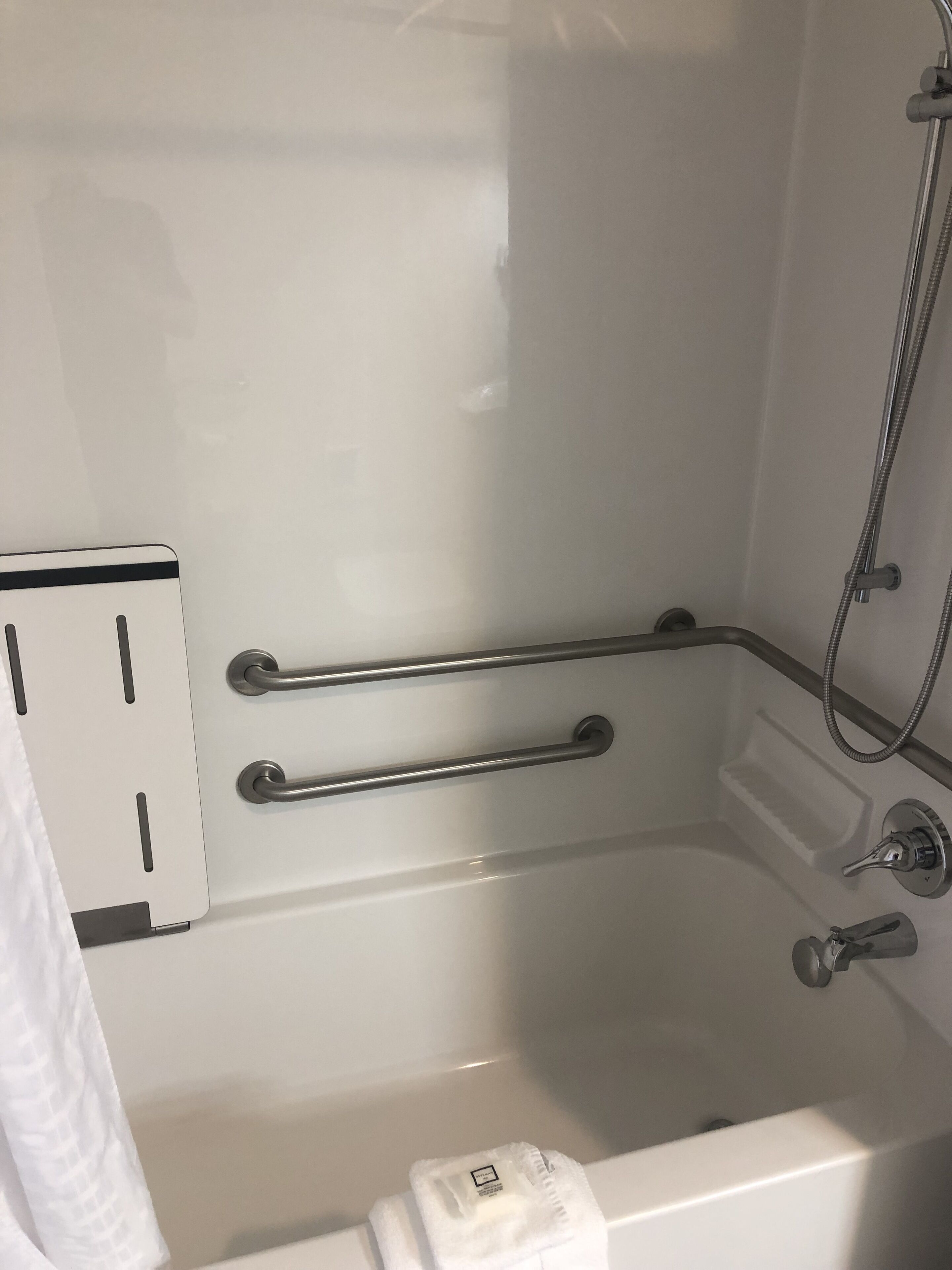 Une baignoire blanche équipée d’un pommeau de douche et de barres d’appui.