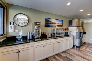 Una cocina con reloj, cafetera, microondas, refrigerador y un cuadro en la pared.