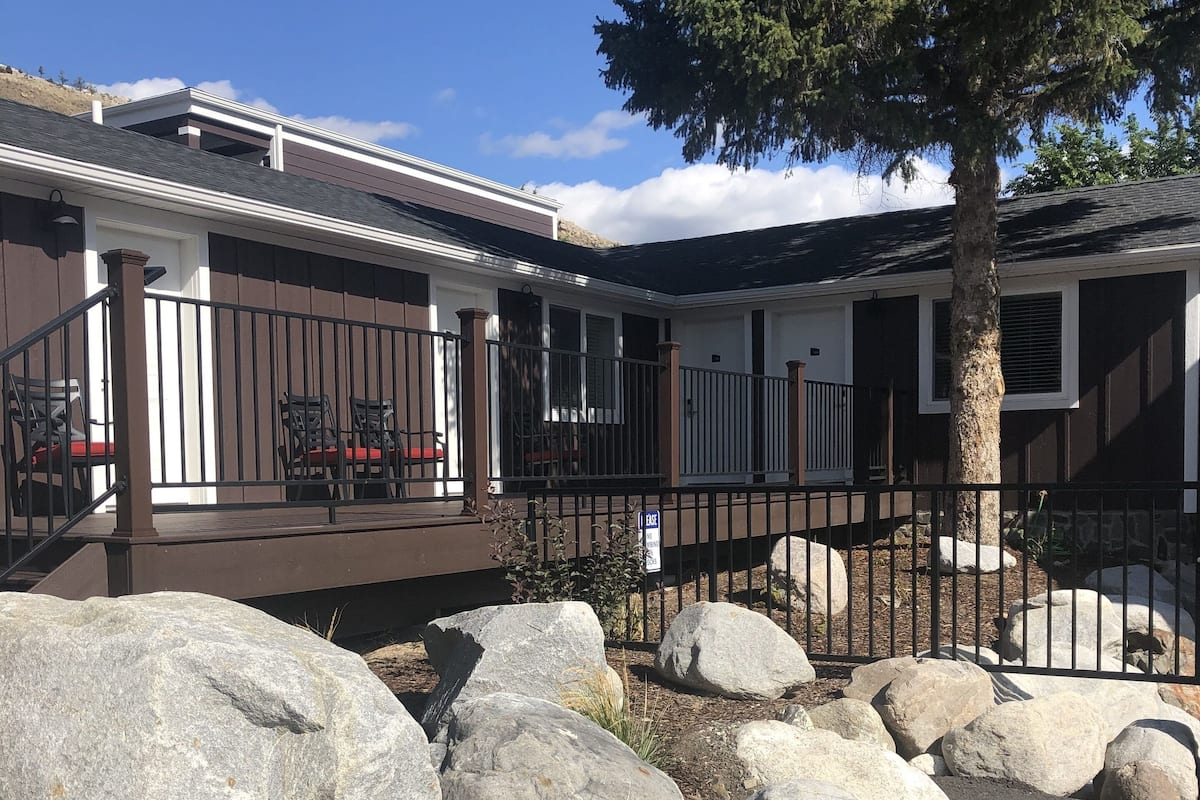 A building with a covered patio area, large rocks in the foreground, and a tree to the right.