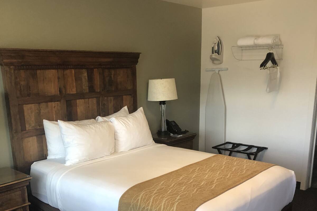 A hotel room with a large bed, a wooden headboard, a bedside table with a lamp, and a wall-mounted air conditioning unit.