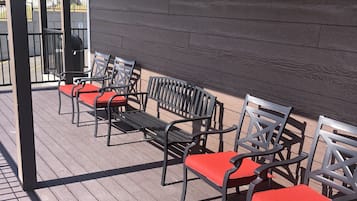 An outdoor seating area with wooden flooring and metal chairs with red cushions.