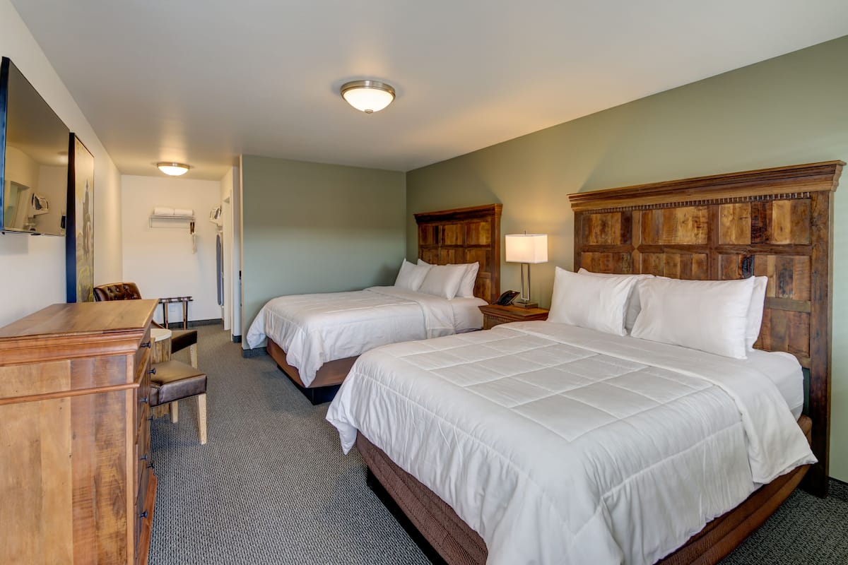 A hotel room with two beds, a wooden dresser, a desk, and a chair.