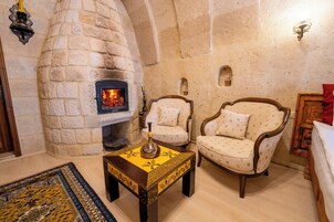 Una chimenea de piedra con fuego, dos sillones tapizados, una mesita con un jarrón decorativo y una alfombra estampada.