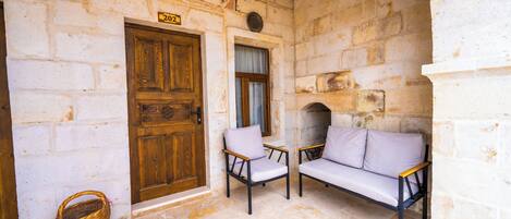 Una habitación con paredes de piedra, una puerta de madera, dos sillas, un sofá y una cesta de mimbre.
