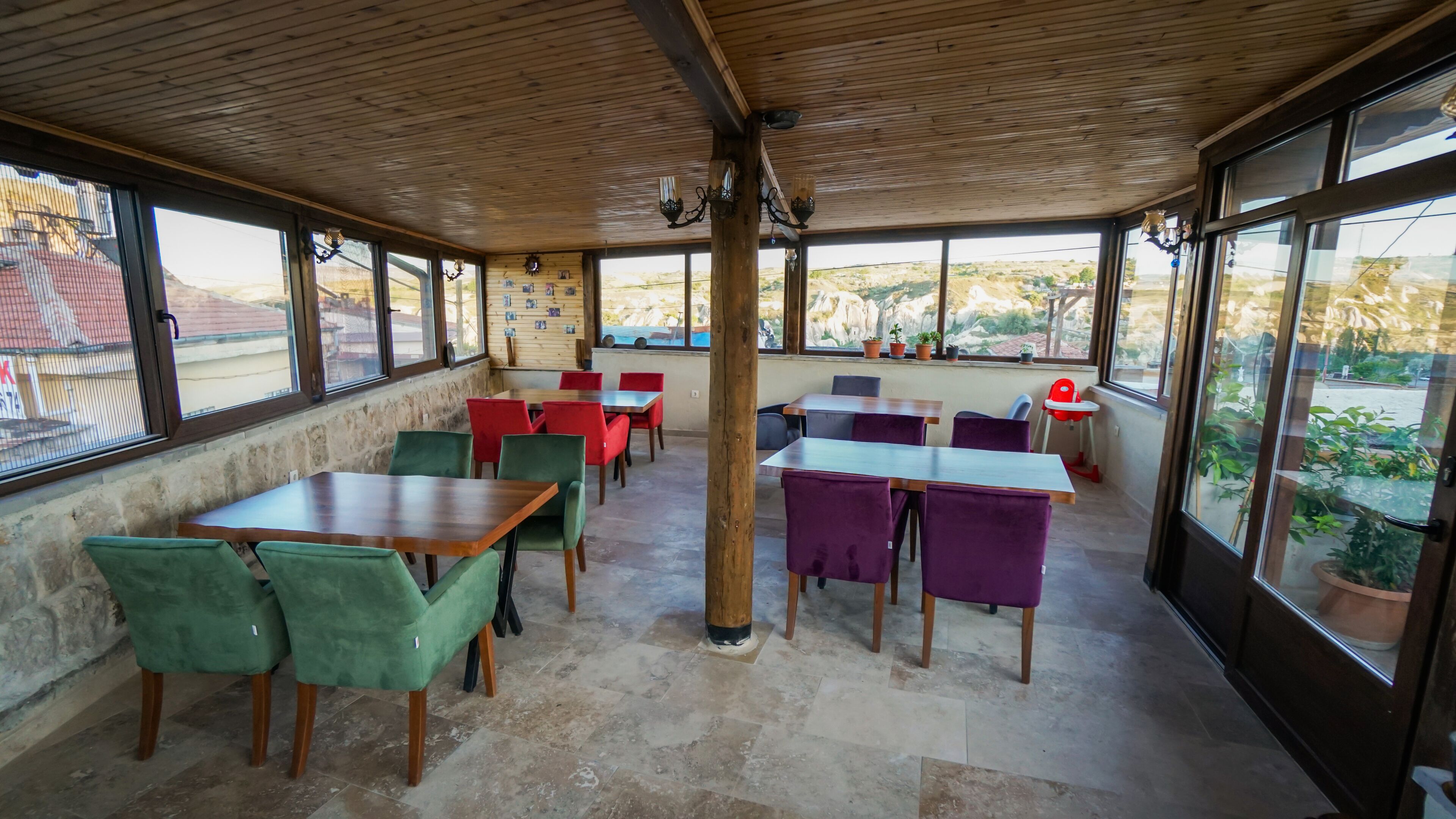 Ein Restaurant mit Holzbalkendecke, großen Fenstern und roten sowie grünen Stühlen.