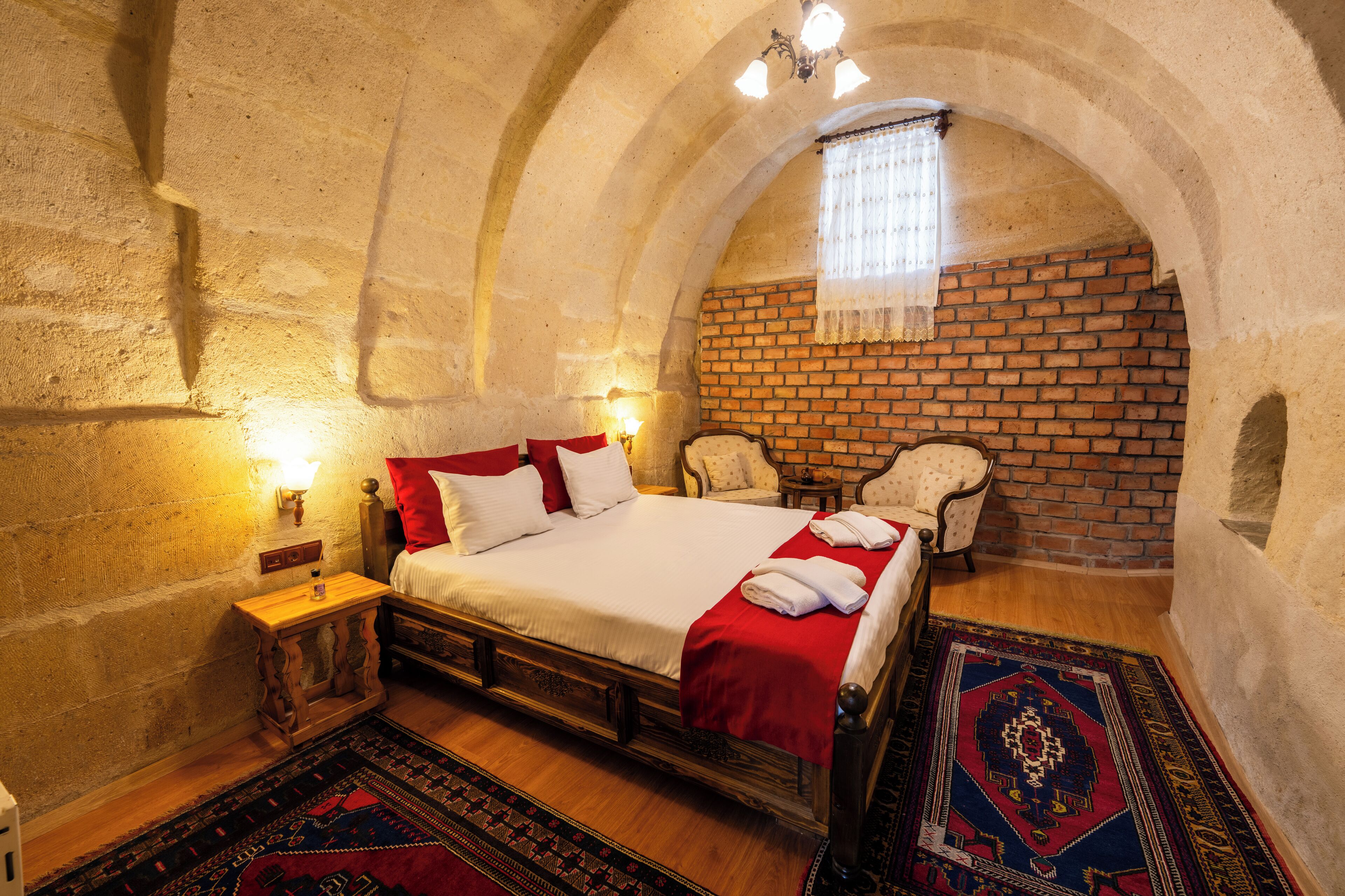 Une chambre à coucher avec un lit en bois, une couvre-lit rouge et blanche, un mur en briques et un lustre.