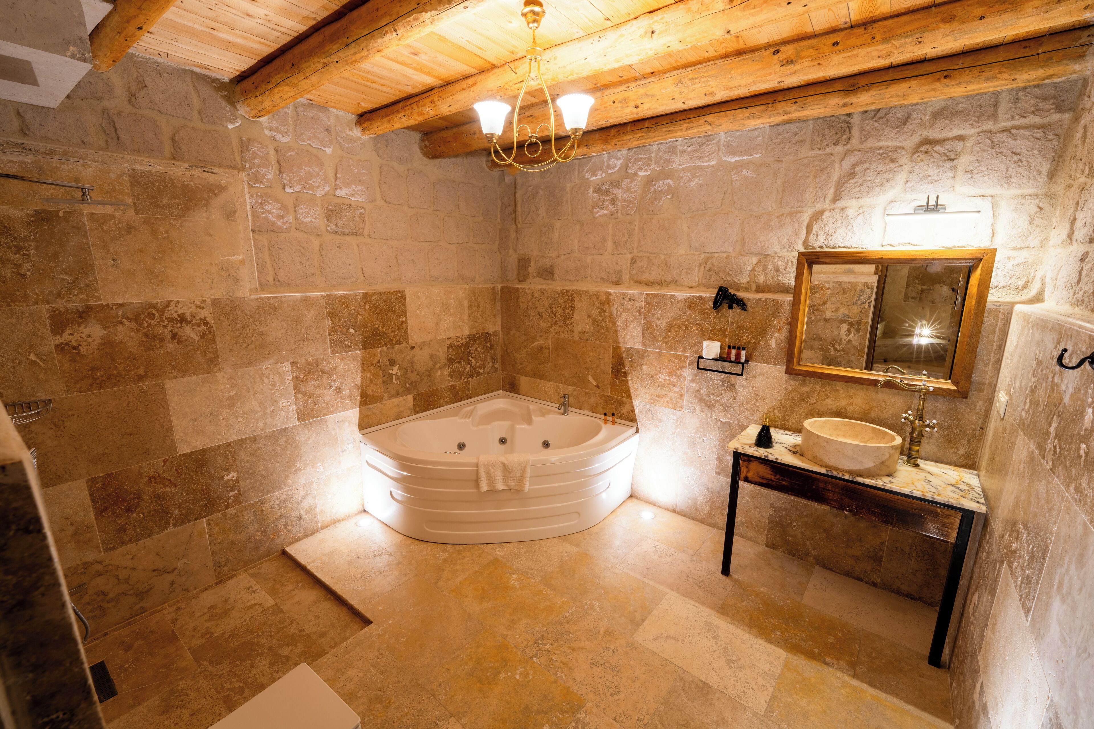 Un baño con pared de piedra, techo de madera, bañera, lavamanos y espejo.