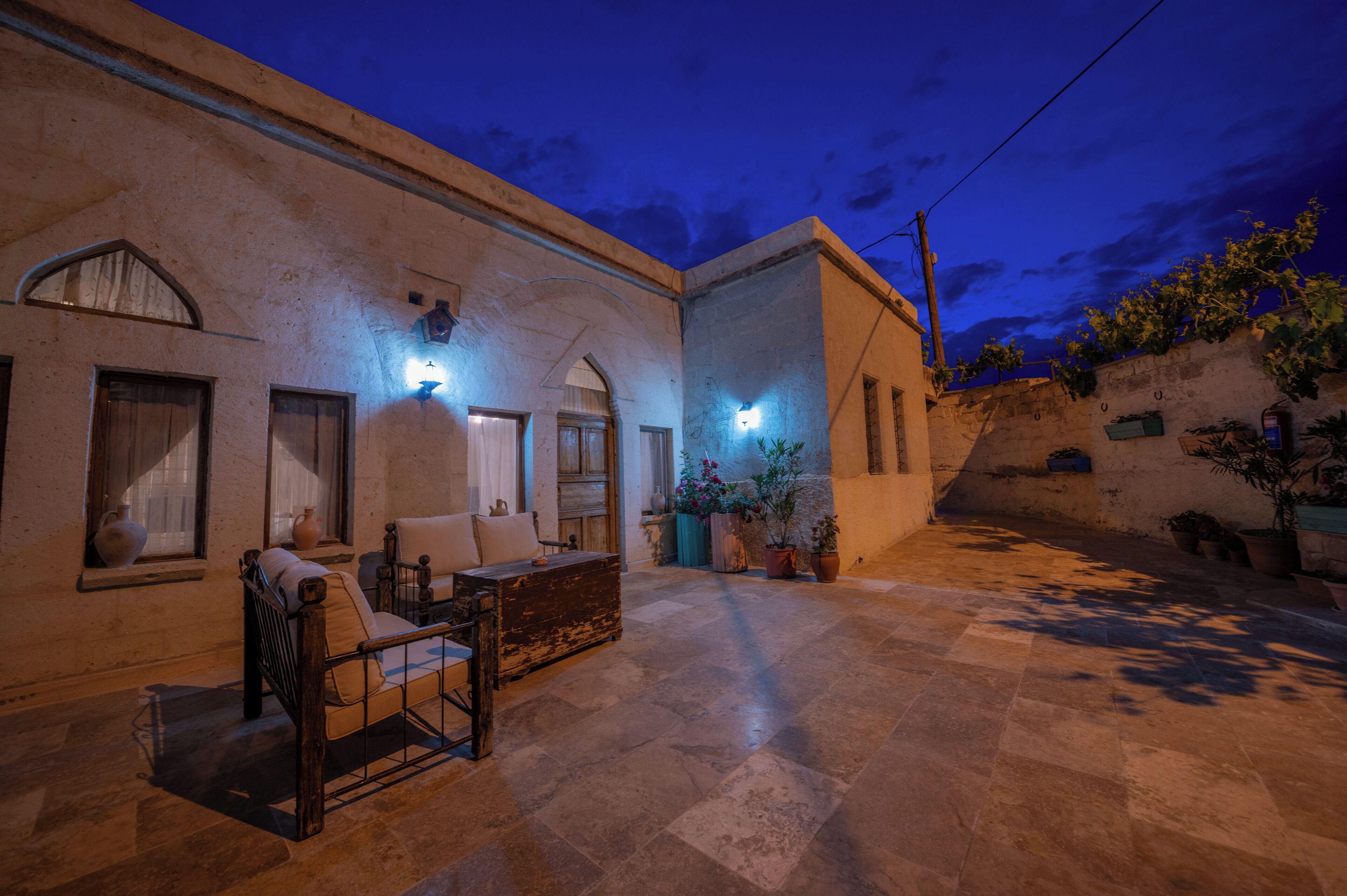 A courtyard with a bed, a table, and chairs, surrounded by walls and potted plants.