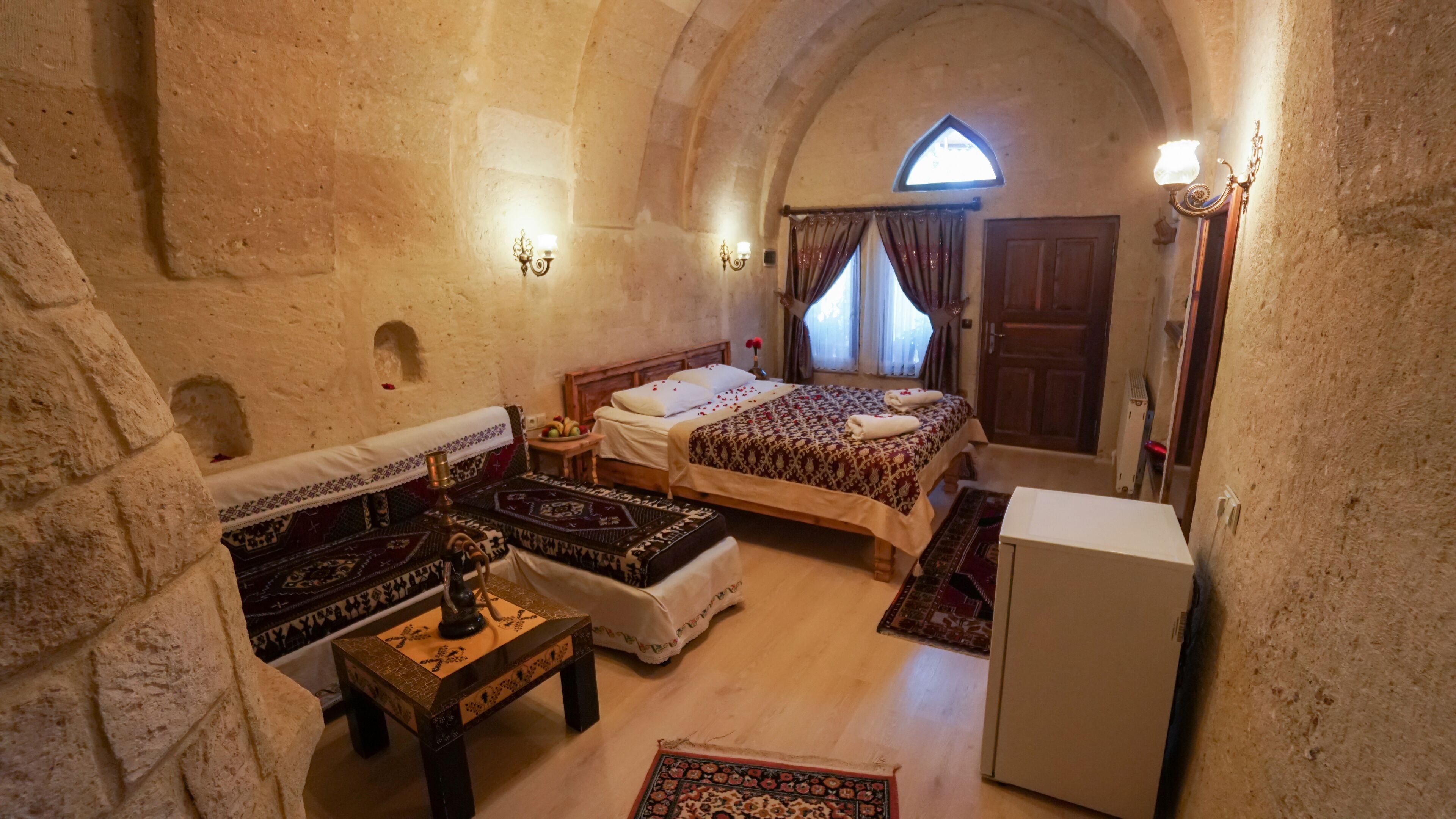 A cozy room with two beds, a small table, and a refrigerator.