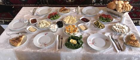 A dining table set with various dishes, including bread, cheese, and vegetables, surrounded by traditional patterned cushions.