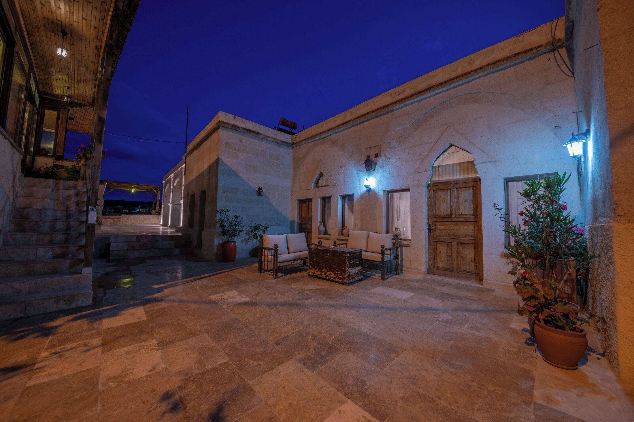 Un patio exterior con suelo de piedra, un banco de madera y una planta en maceta.