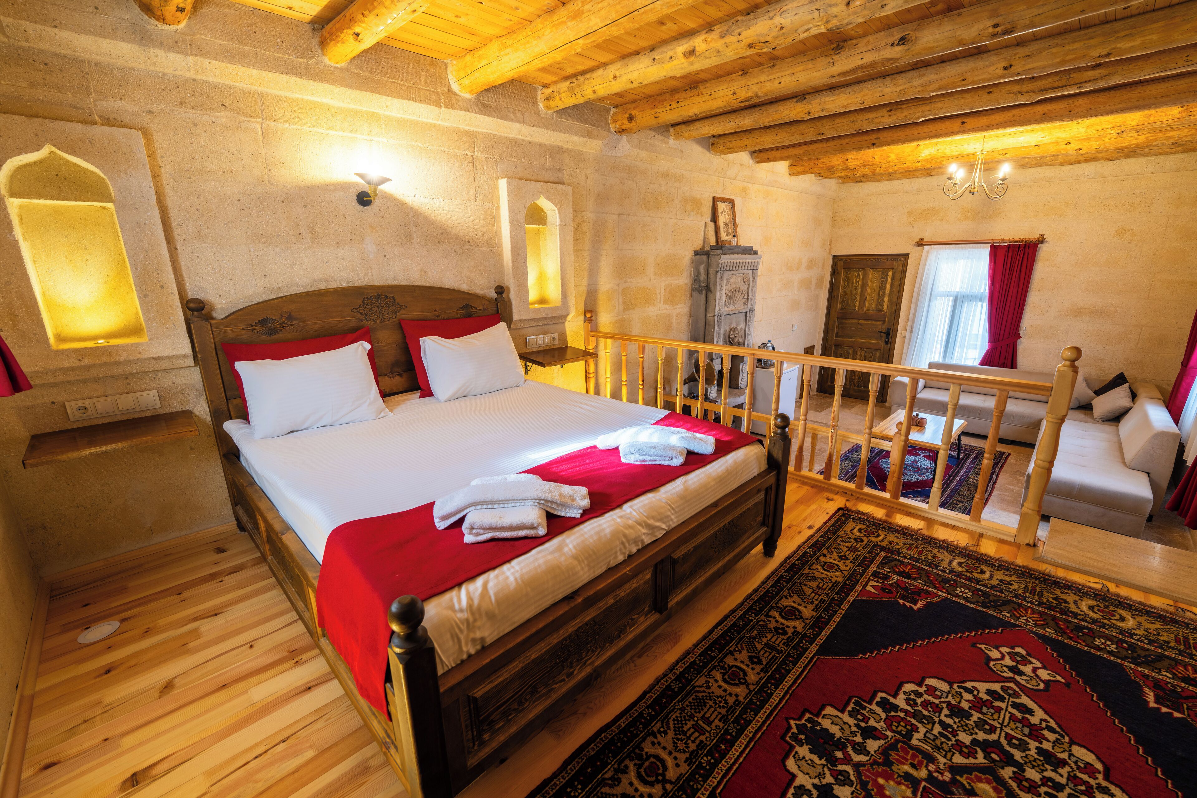A wooden-framed bed with white linens and red accents, a wooden floor, and a traditional rug.