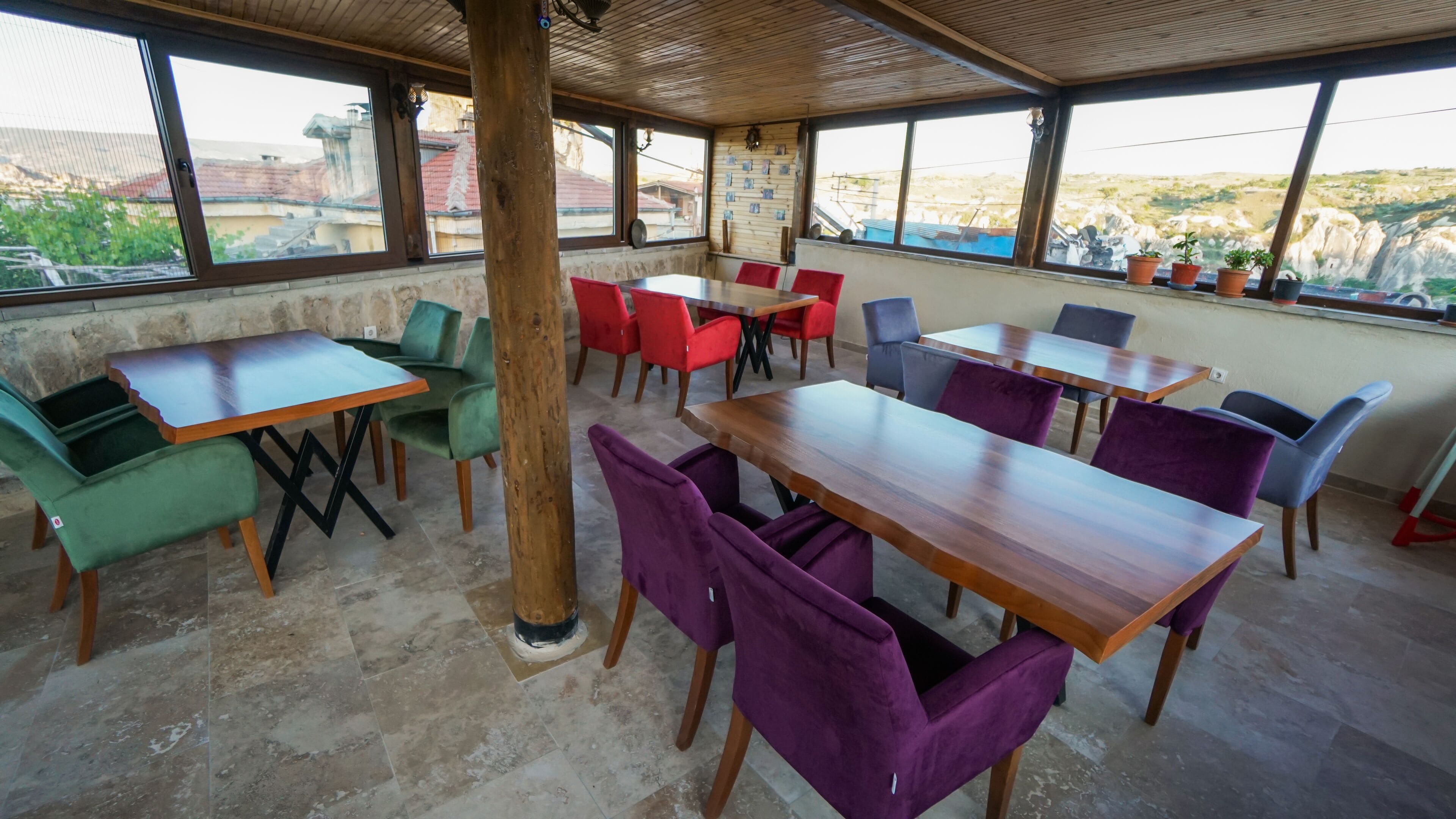 Un restaurante con varias mesas y sillas, amplias ventanas que ofrecen vistas del paisaje, y un techo de madera.