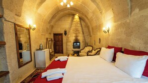 A hotel room with a stone arch ceiling, a fireplace, a bed with red bedding, a mirror, and a small table with a lamp. - Asyada Suites Hotel (Ürgüp)