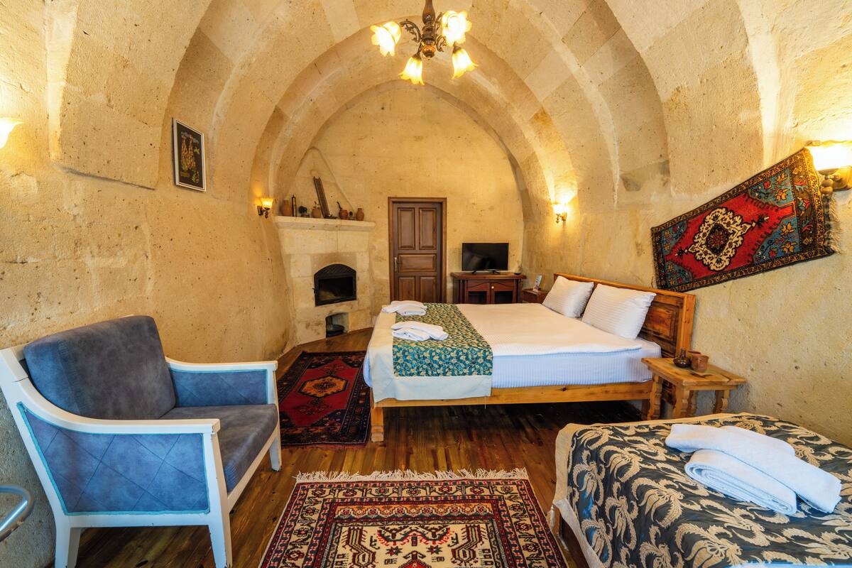 A bedroom with a wooden bed, a chair, a sofa, a fireplace, and a large arched stone ceiling.