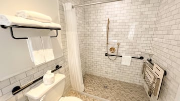 A modern bathroom with white subway tiles, a beige herringbone floor, a glass shower enclosure, and a toilet with a grab bar.